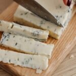 a person cutting gorgonzola cheese