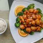 piatto di pollo cinese all'arancia su base di broccoli vicino ad una scodella di riso bianco