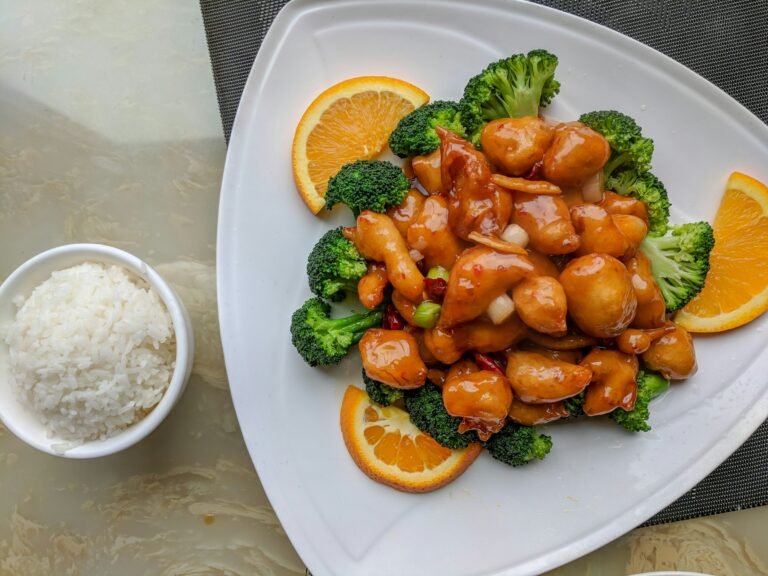 piatto di pollo cinese all'arancia su base di broccoli vicino ad una scodella di riso bianco